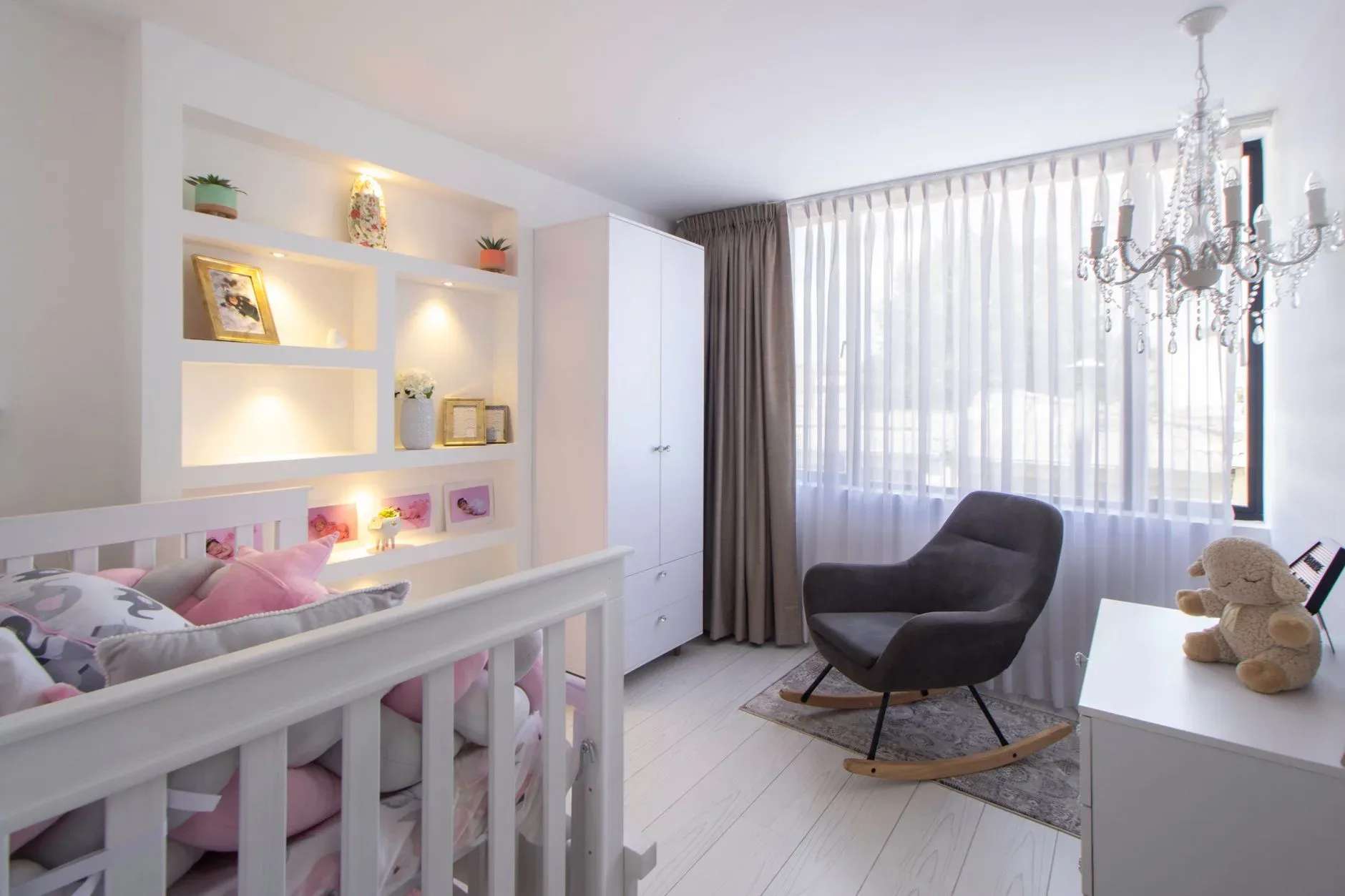 A bright and modern children\'s room with a crib, armchair, and chandelier.