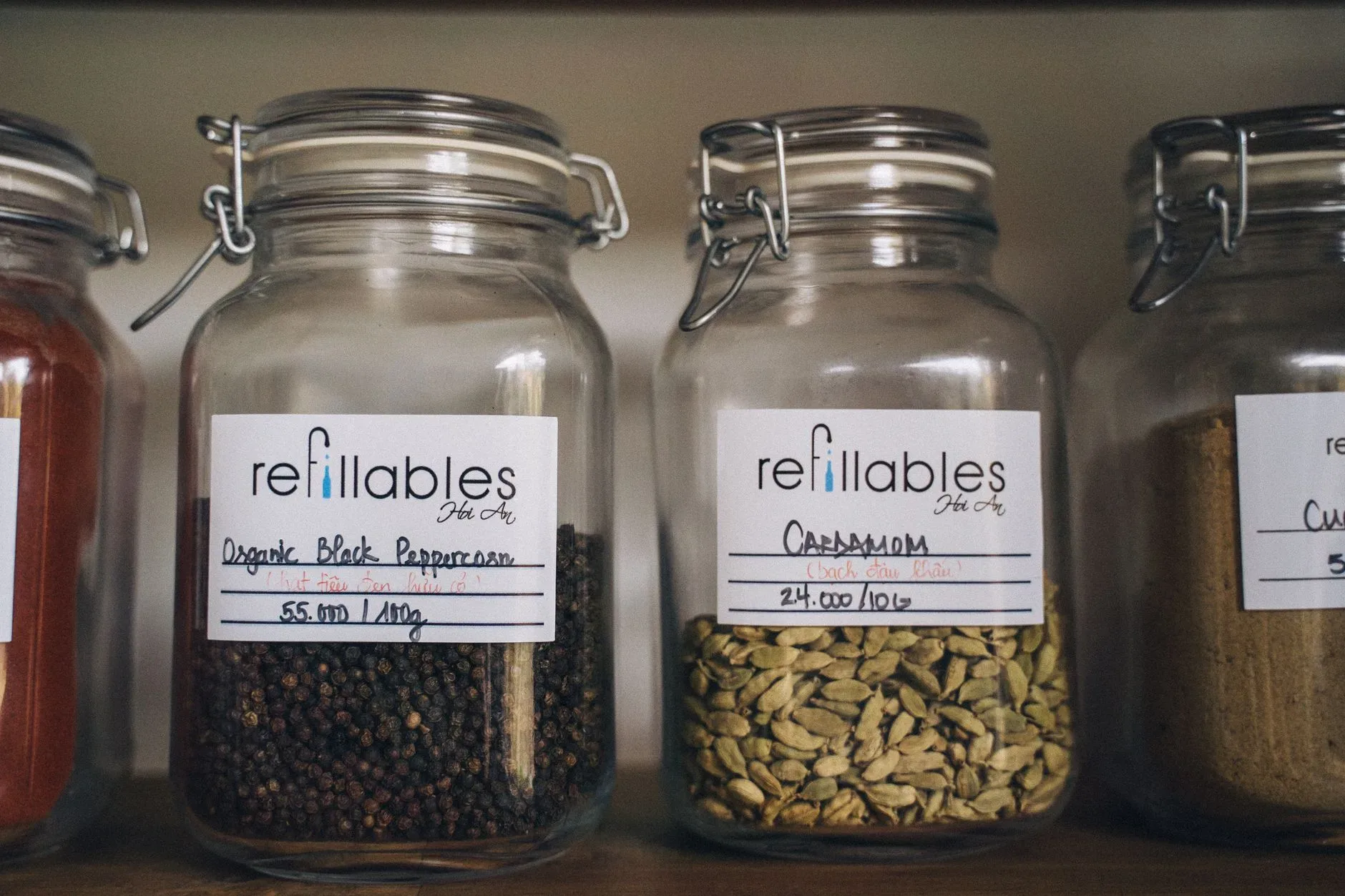 A collection of spices in eco-friendly refillable glass jars on a wooden shelf, promoting sustainable food storage.