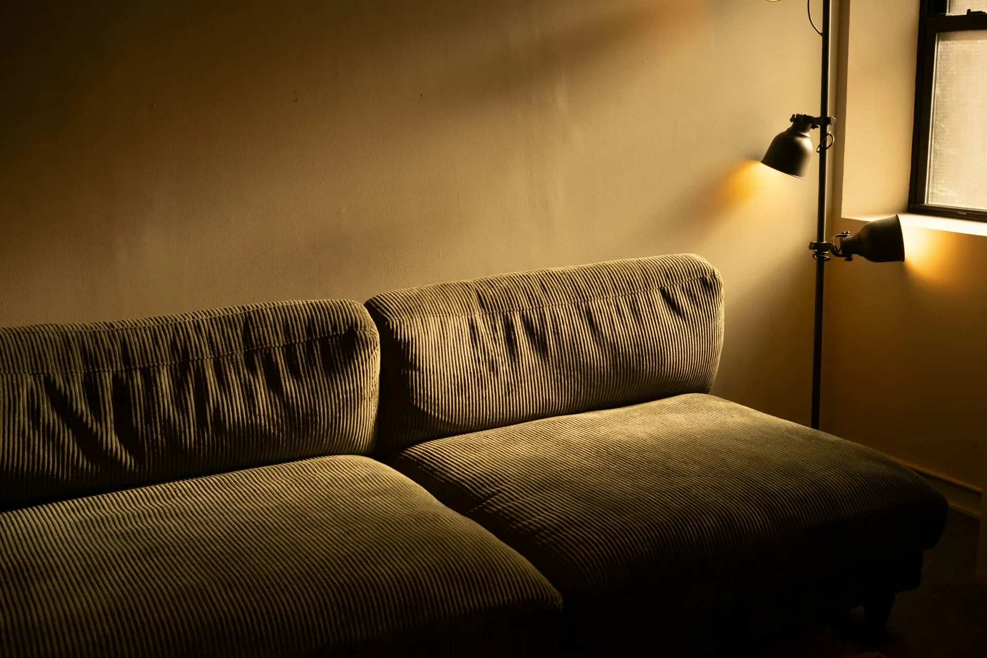 A dimly lit sofa with a floor lamp behind it.