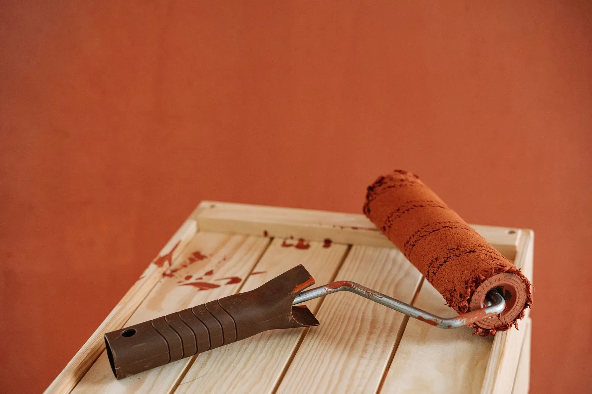 A paint roller with rustic brown paint on a wooden surface against an earthy wall.