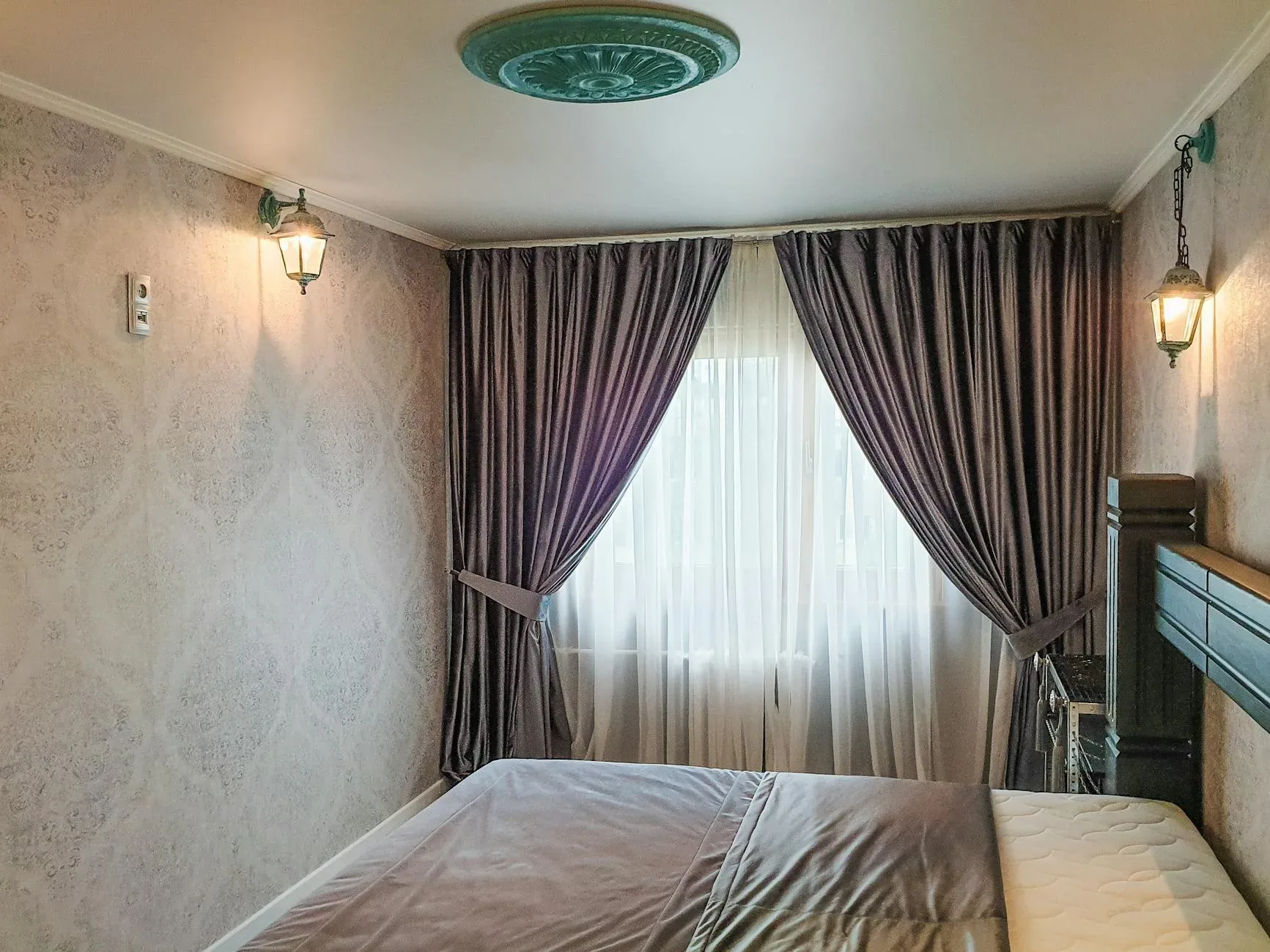 A serene bedroom featuring elegant curtains and classic wall sconces.