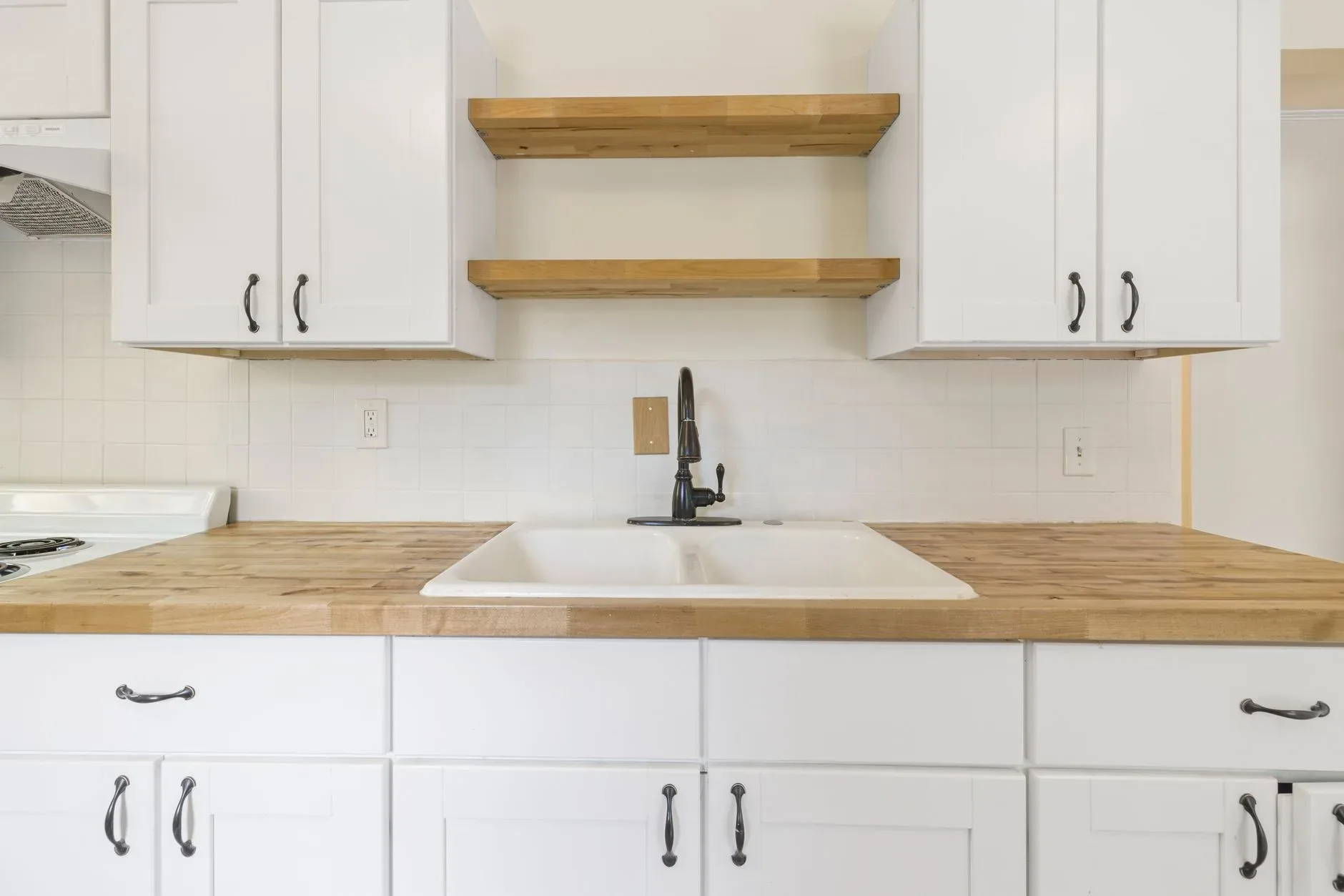 A spacious, modern kitchen with white cabinets and wood countertops.
