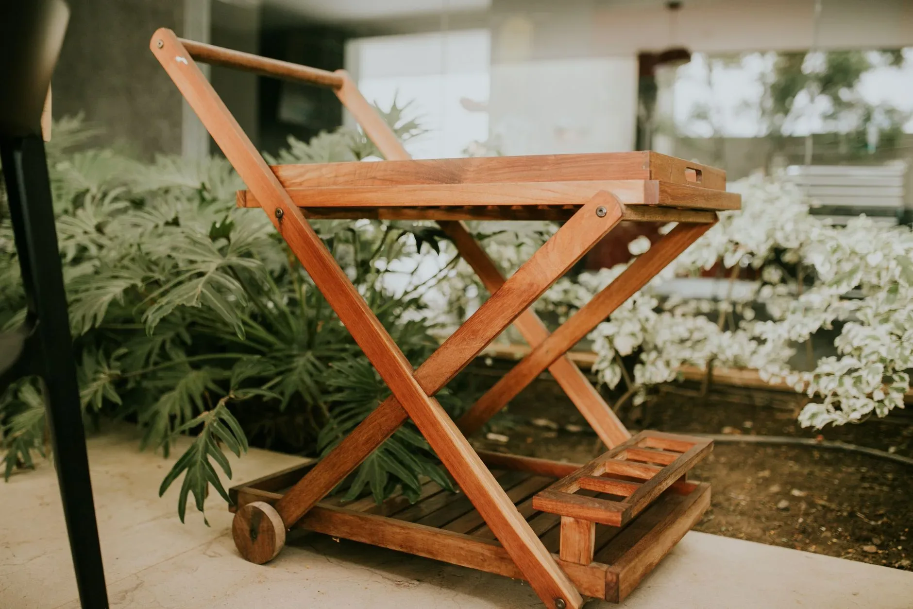 A stylish wooden serving cart placed amid lush greenery in a modern indoor setting.