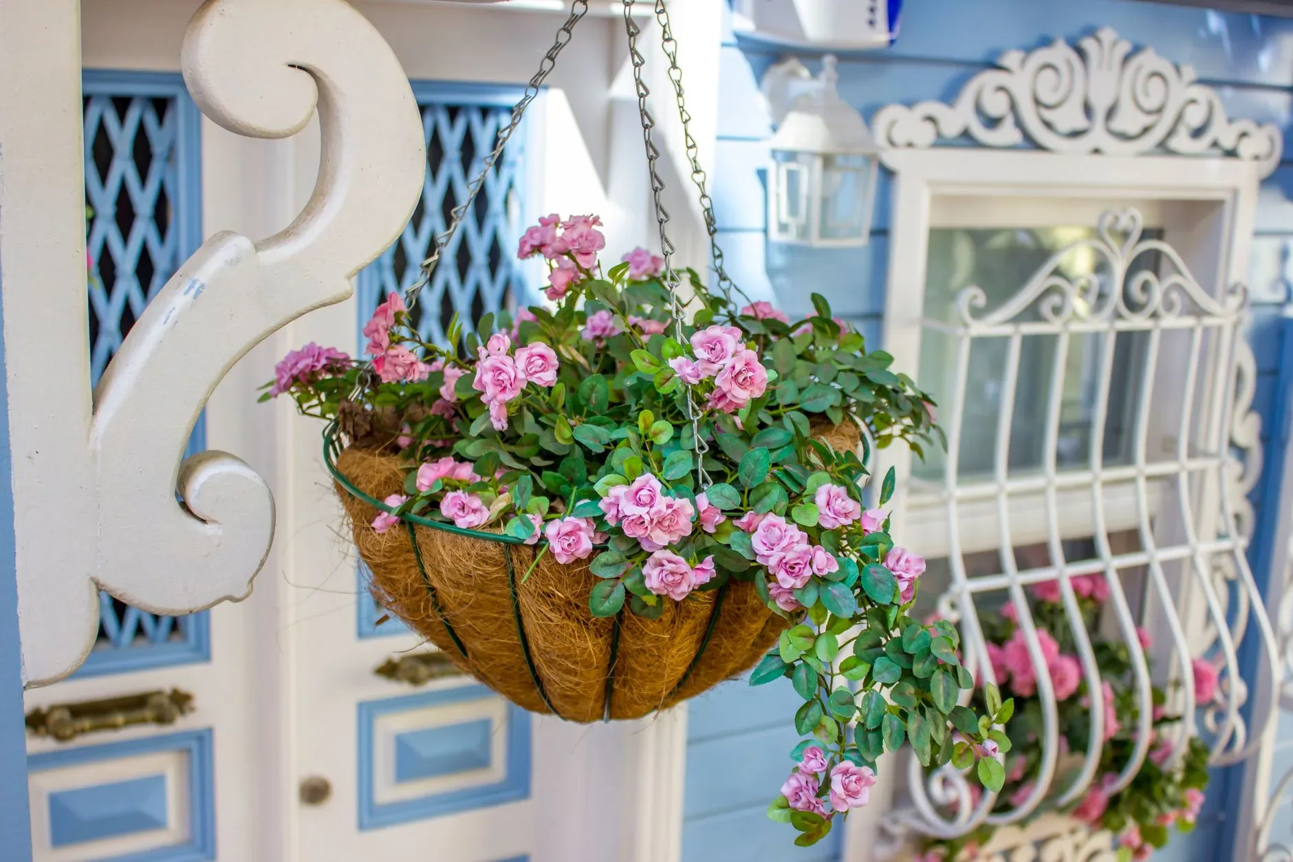 Beautiful pink flowers bloom in a hanging basket on a quaint porch with intricate white designs.