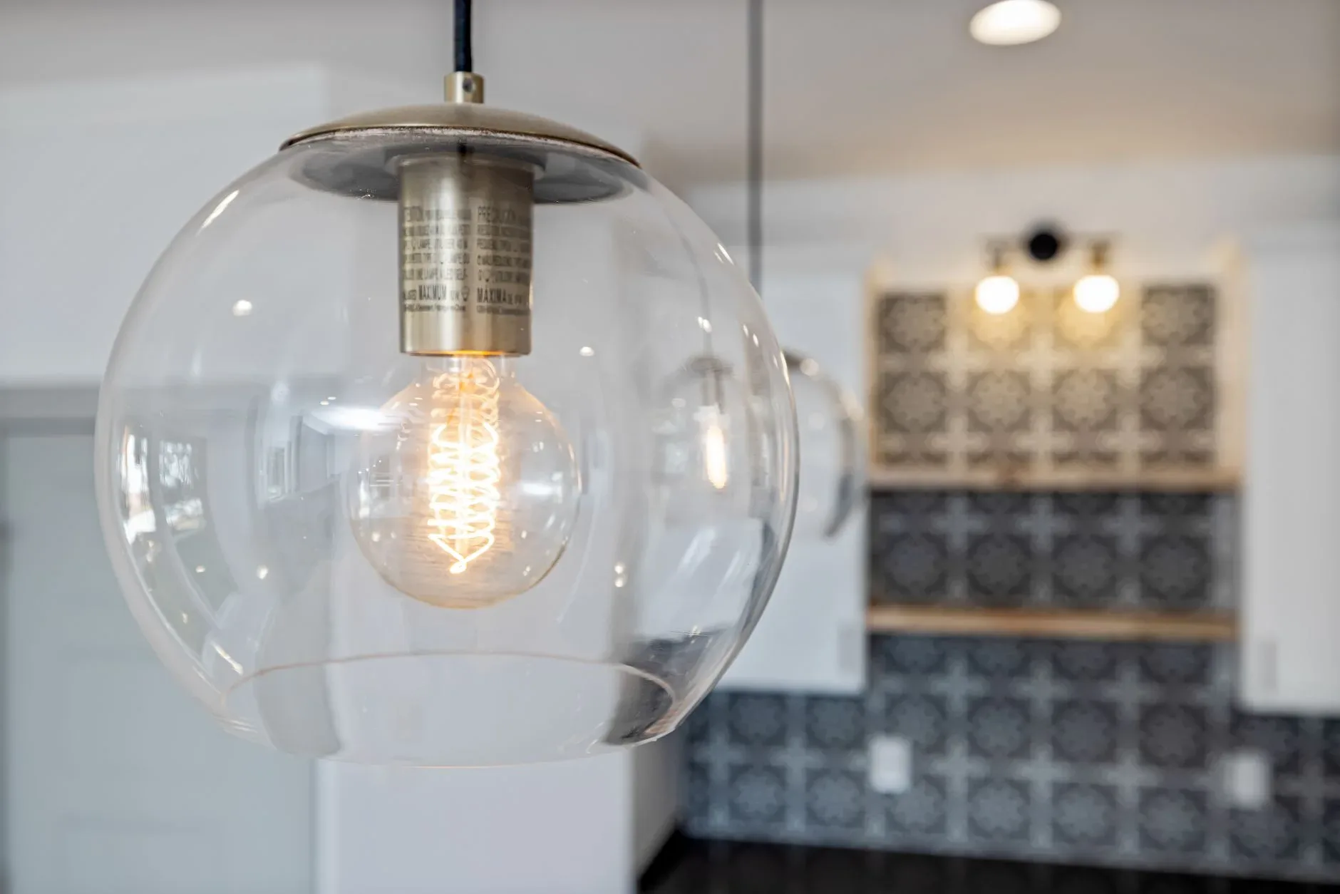Close-up of a glass pendant light bulb illuminating a stylish, modern kitchen interior.