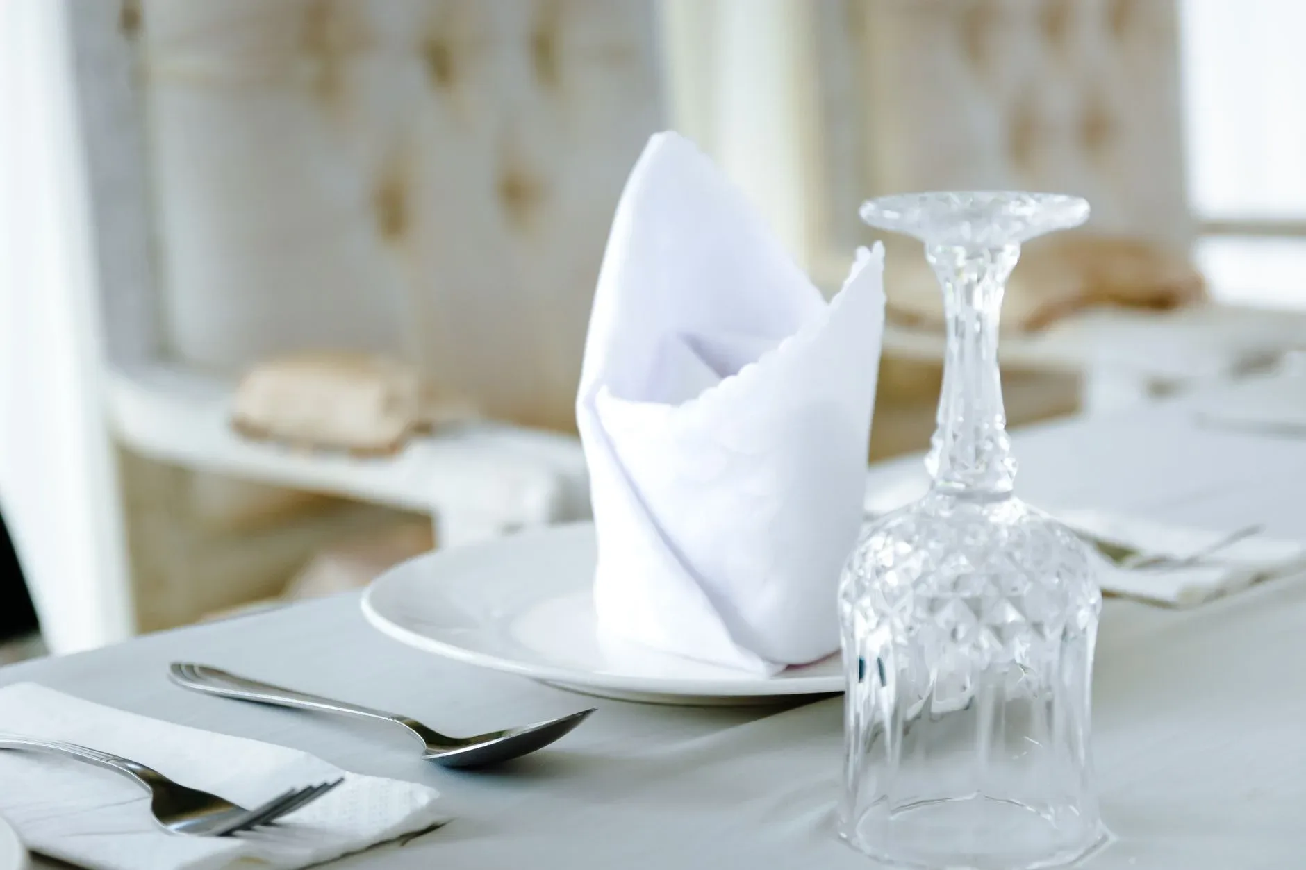 Close-up of an elegant table setting featuring a crystal glass and folded napkin on a plate.