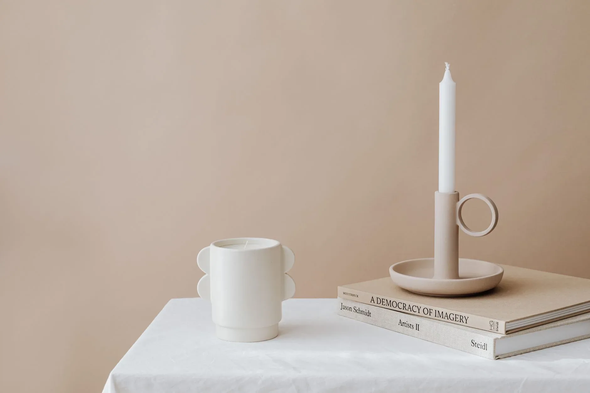 Elegant still life with candleholder, mug, and books on a beige backdrop. Perfect for minimalist decor.