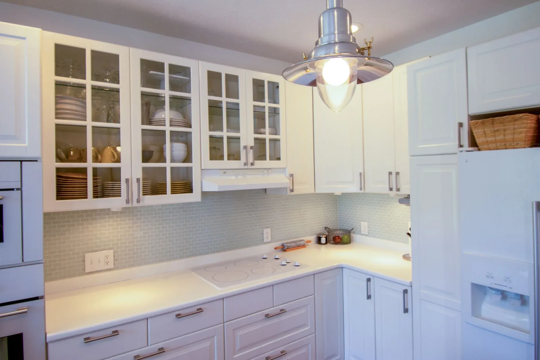Elegant white kitchen with glass cabinets and modern appliances in an open layout.