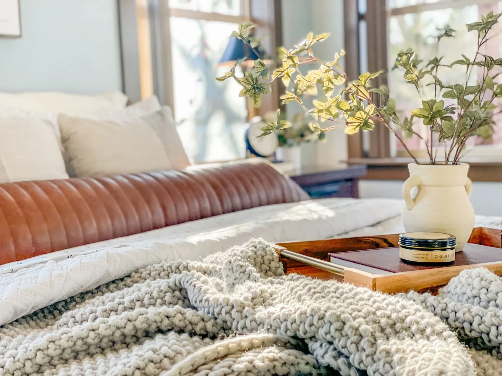 Inviting bedroom setup featuring a knitted blanket, ceramic vase, and green plant on a cozy bed tray.