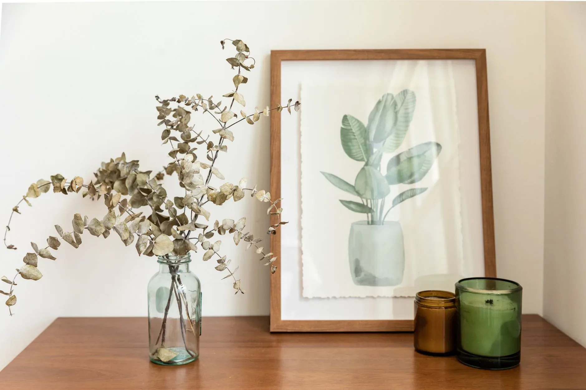 Minimalist interior with a eucalyptus arrangement, framed botanical print, and candles.