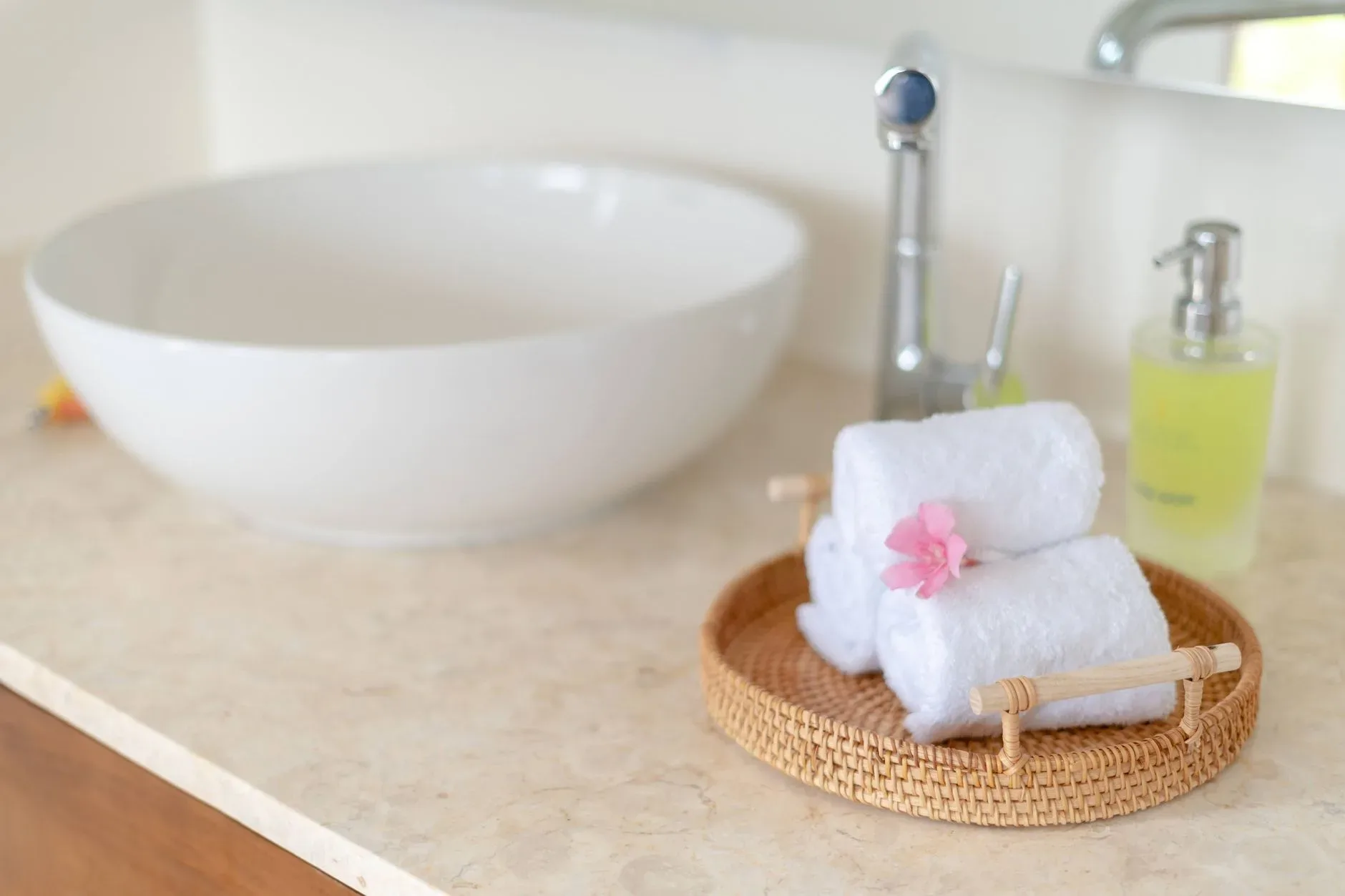 Serene bathroom featuring rolled towels, a bowl sink, and soap dispenser.