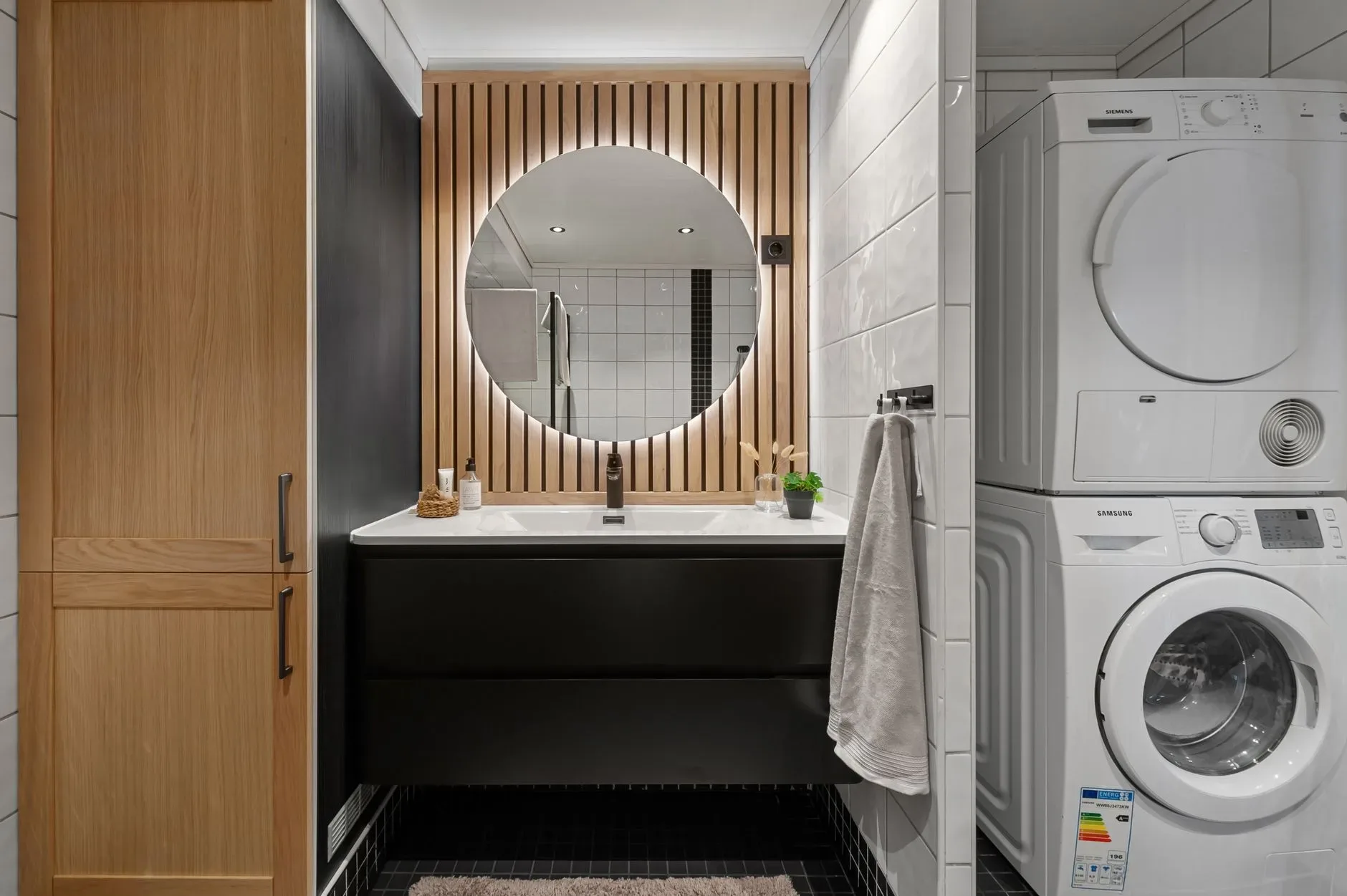 Sleek bathroom featuring a round mirror, modern sink, and integrated washer and dryer.