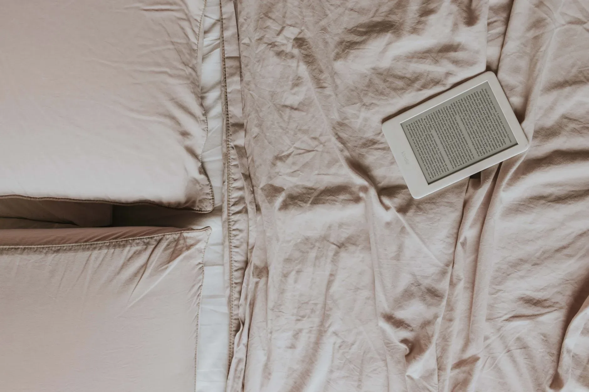 Top view of a cozy bed with an ebook reader on soft sheets, perfect for relaxed reading enthusiasts.