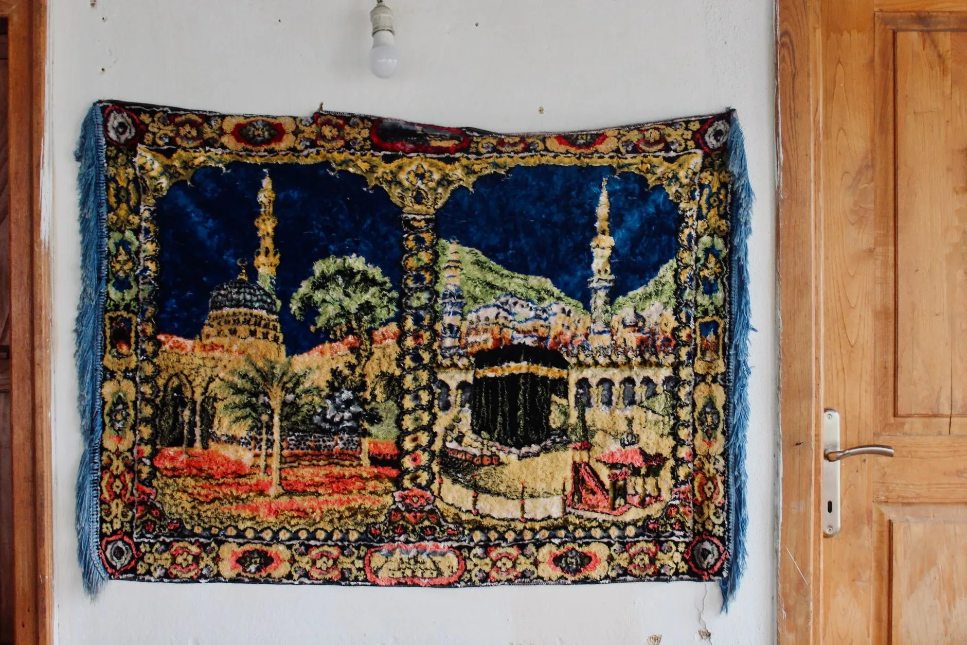 Vibrant tapestry featuring mosque and minarets hung on white wall indoors.