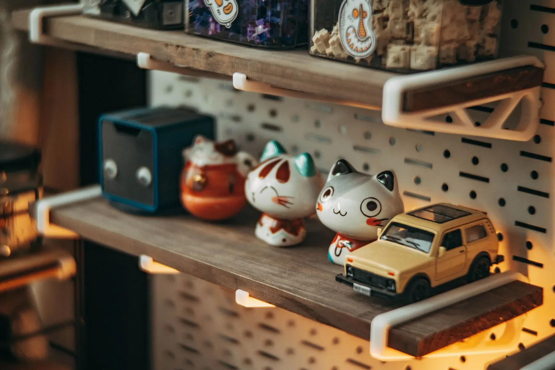 Wooden shelf with cute cat figurines and toy car, soft ambient lighting.